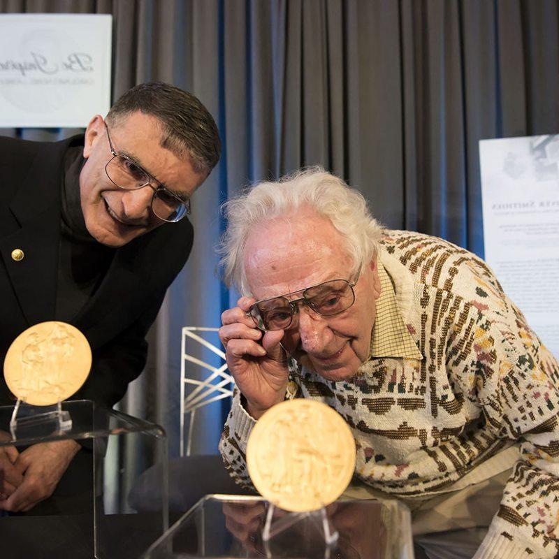 奥利弗·史密斯和阿齐兹·桑卡尔看着他们的诺贝尔奖奖牌.