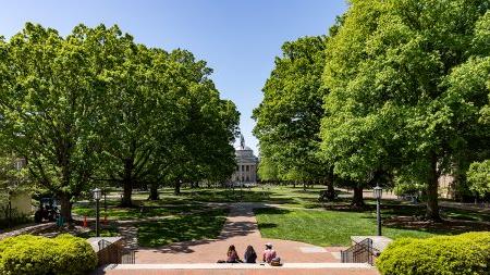 Three students sitting on the steps of South Building overlooking main campus quad.